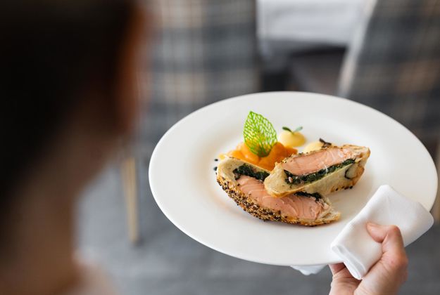 Ein Kellner serviert ein Hauptgericht in unserem Sporthotel in den Dolomiten